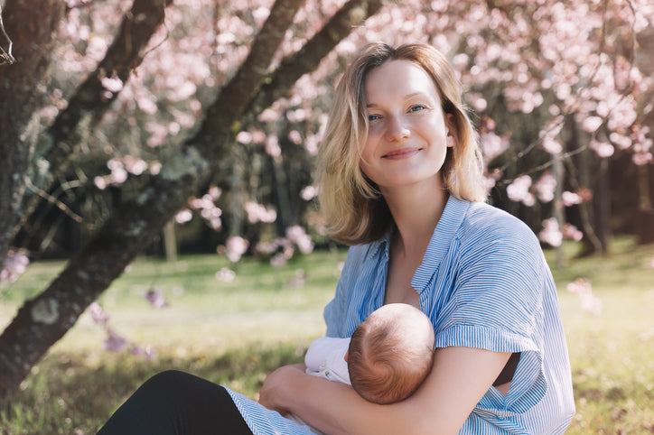Smiling mother breastfeeding her baby outdoors under a blossoming tree