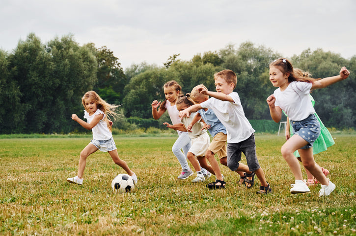 kids playing soccer outdoors with Dr. Nice’s Kids Sports Gel in background