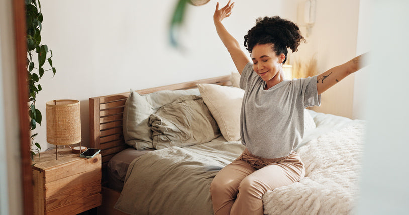 Woman stretching her arms happily while sitting on her bed